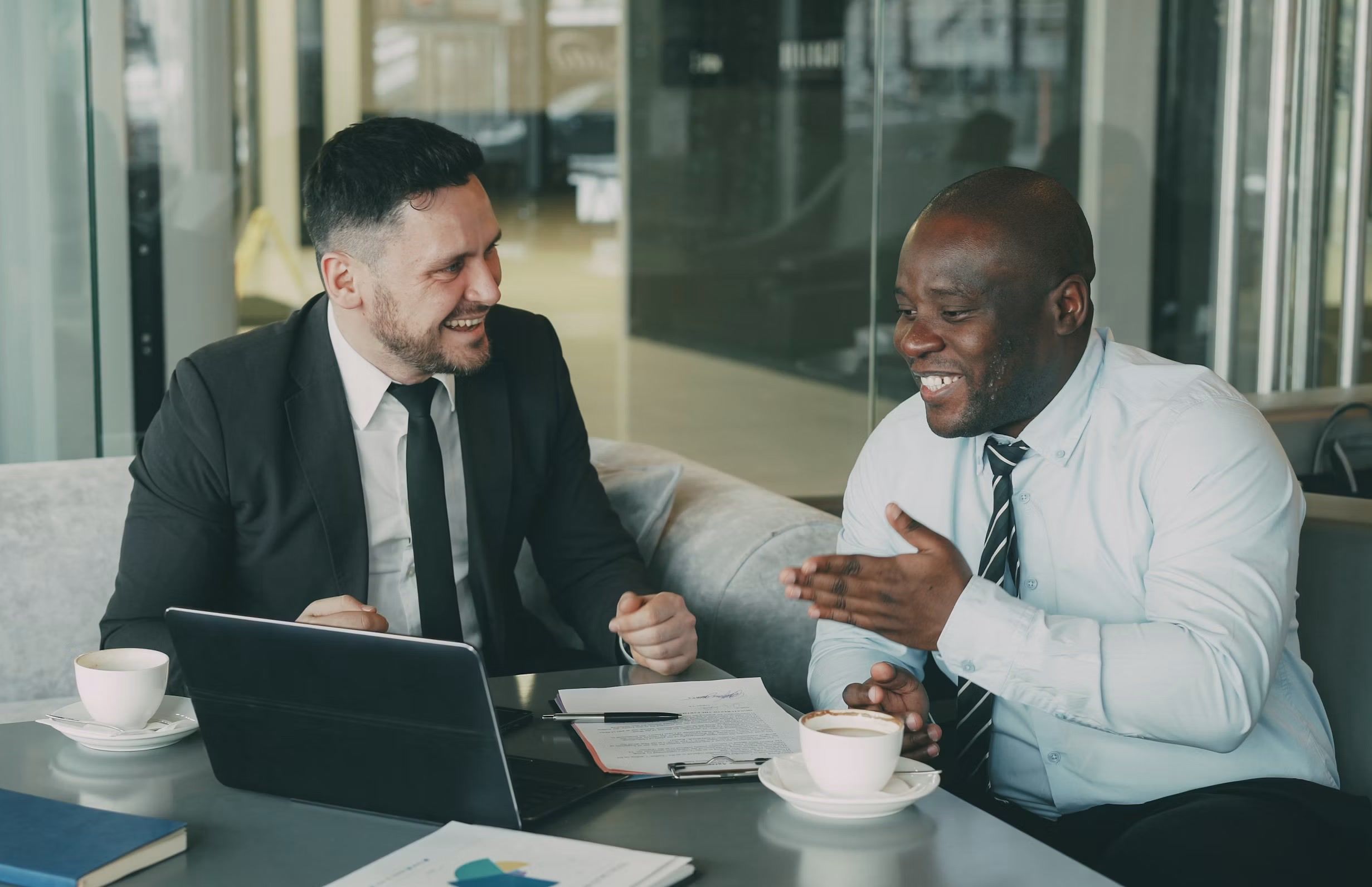 Two businessmen talking over coffee and a laptop